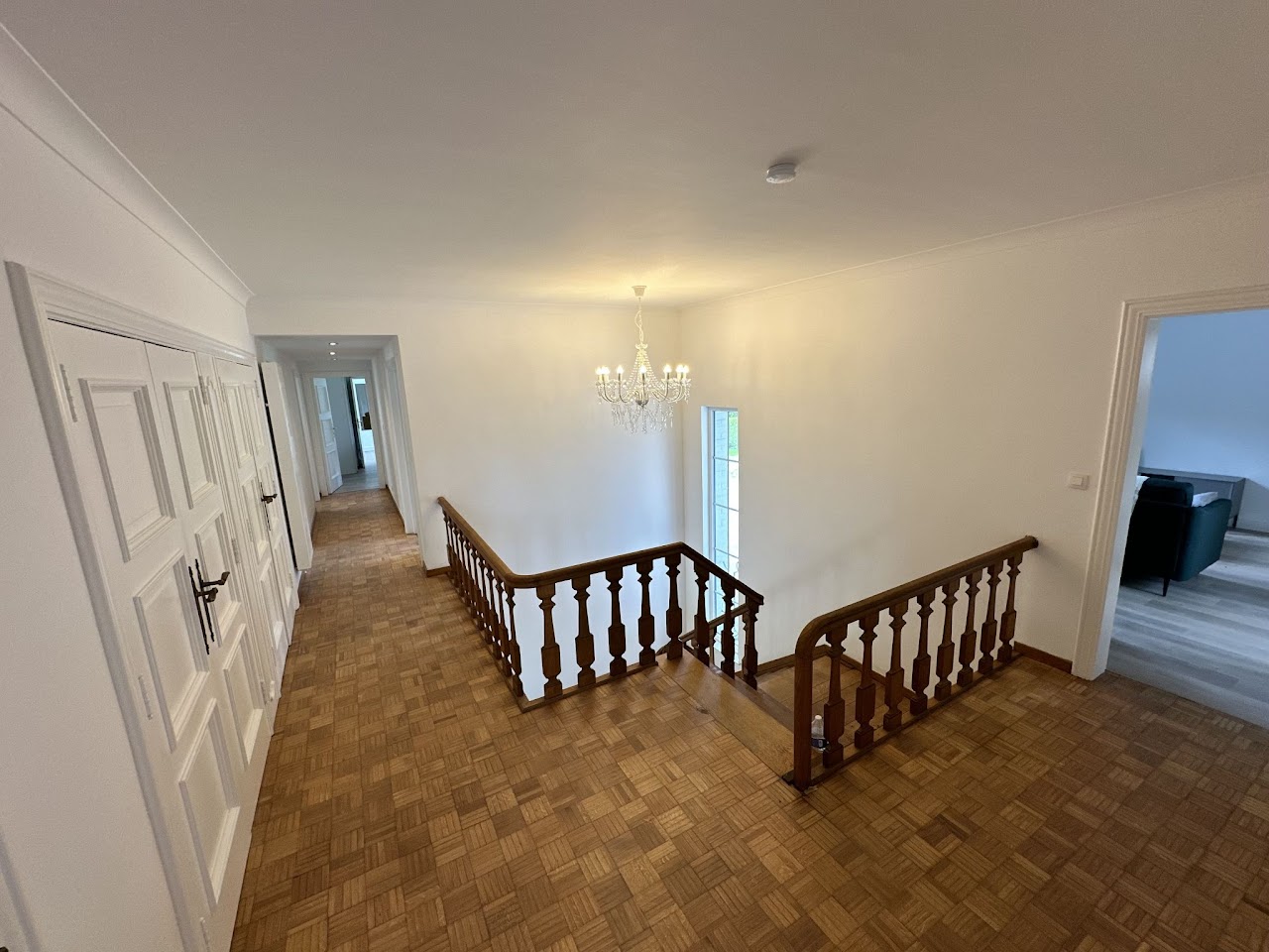 Palier à l'étage avec escalier en bois et lustre élégant, villa Domaine de la Chênaie